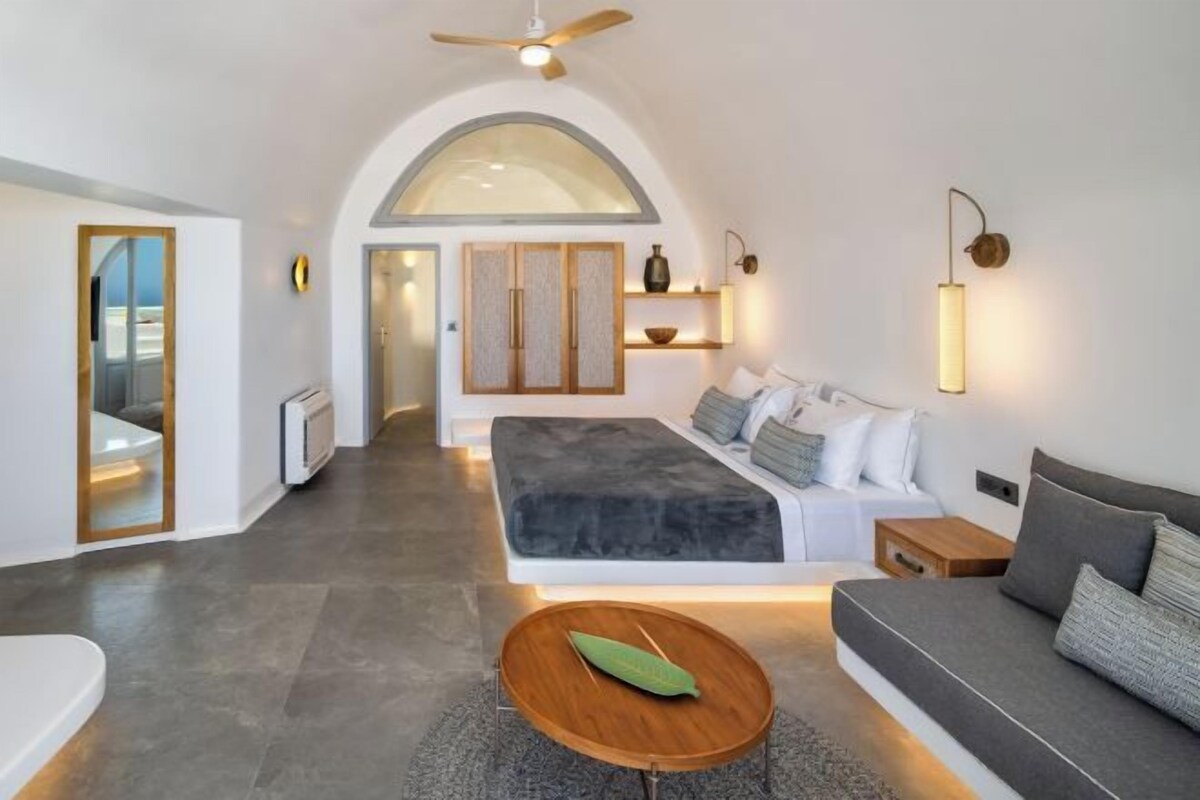 A modern bedroom with a bed, a sofa, a small table, and a ceiling fan.