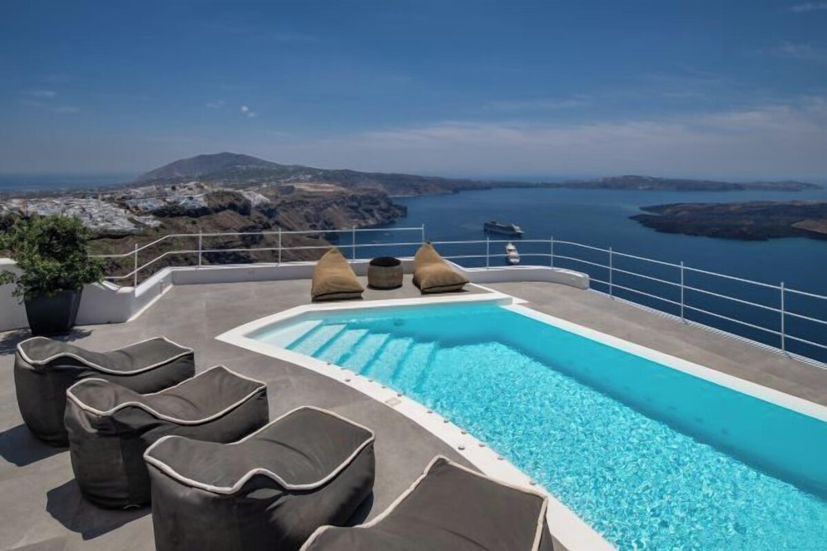 A rooftop infinity pool with lounge chairs and a view of the sea and mountains.