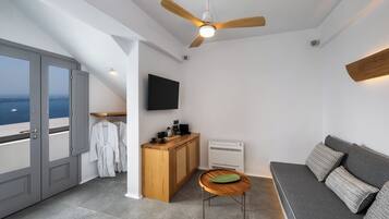 Ett modernt rum med en balkong, en takfläkt, en platt-TV, en soffa, ett litet bord och ett litet kök.