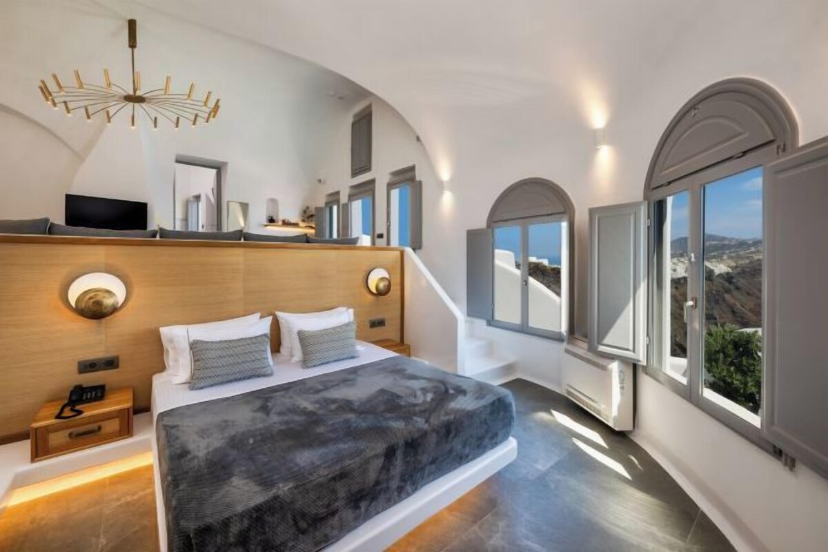 A modern bedroom with a large bed, a TV, and a view of the landscape.