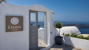 A white building with a sign reading "Eteoro Suites" and a view of the sea. - Eteoro Suites (Santorini)