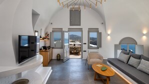 A modern interior with a TV, sofa, and dining area. - Eteoro Suites (Santorini)
