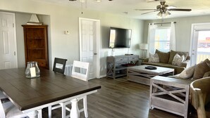 A living room with a wooden dining table, white chairs, a sofa, and two ceiling fans.