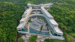 A modern hotel with a unique curved architecture, multiple swimming pools, and lush surrounding greenery. - Secrets Bahia Mita Surf & Spa (Punta de Mita)