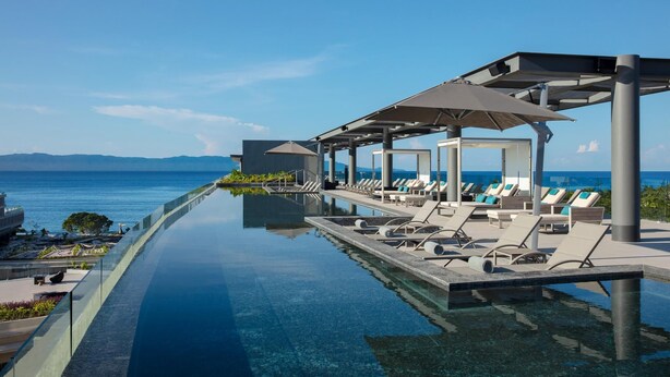 A infinity pool with lounge chairs and umbrellas, overlooking the sea. - Secrets Bahia Mita Surf & Spa (Punta de Mita)