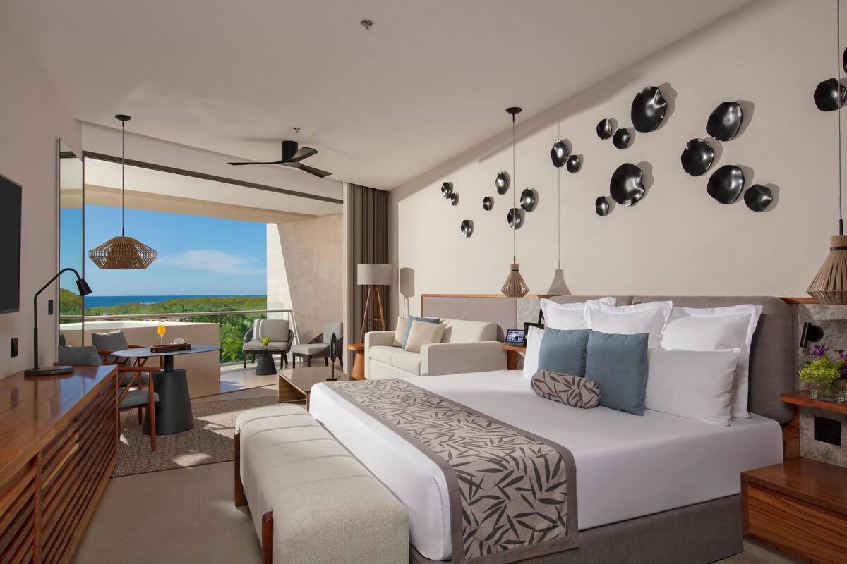 A modern hotel room with a large bed, a desk, and a view of the ocean.