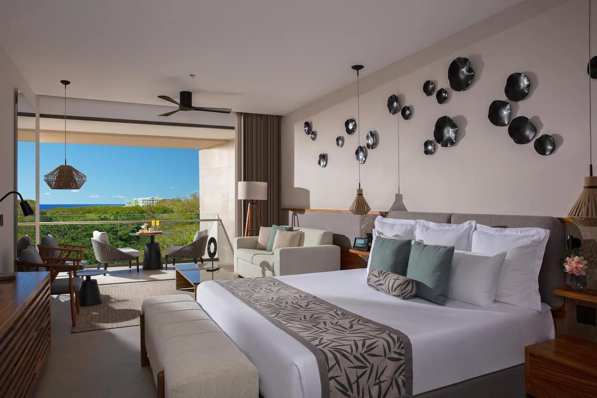 A modern hotel room with a large bed, a balcony with seating, and decorative wall art.