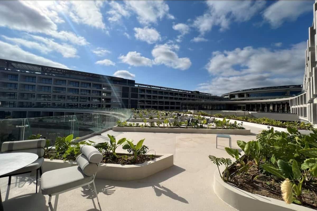 A rooftop terrace with modern outdoor seating, planters with greenery, and a clear view of a multi-story building.