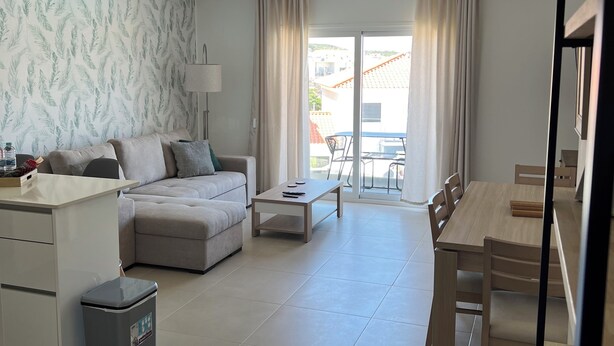 A spacious living area with a sofa, a coffee table, and a dining table with chairs. There is a trash bin and a lamp. The room has a large window with curtains. - Spectacular views and location (Salir do Porto)