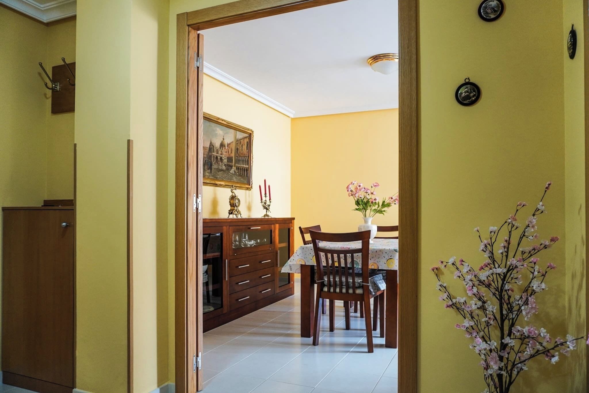 Uma área de jantar com mesa e cadeiras de madeira, um vaso com flores e um aparador com portas de vidro.