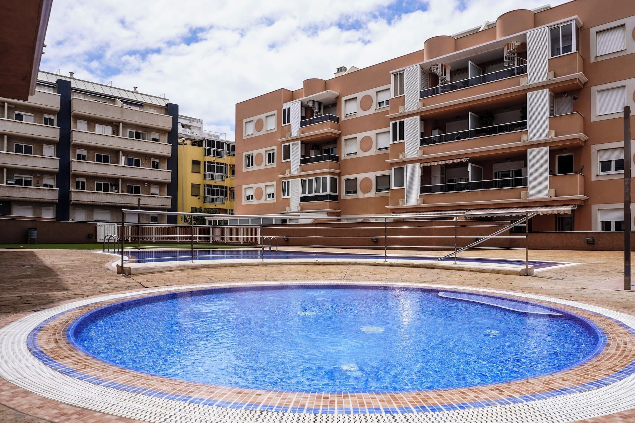 A swimming pool surrounded by multi-story residential buildings with balconies and a clear sky.