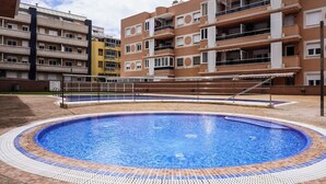 En swimmingpool omgiven av höga bostadshus med balkonger och en klar himmel.