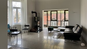 A spacious living room with a high ceiling, large windows, a fireplace, and modern furniture.