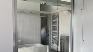 A modern bathroom with a glass shower enclosure, a bathtub, and a walk-in closet with a mirrored closet door.