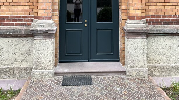 A dark blue double door with a glass panel, a brick facade, and a small step leading to the entrance.