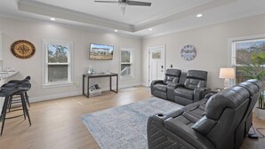 A spacious living room with a ceiling fan, a large grey sofa, a black leather chair, a small table, and a bar stool. - Wait' N Sea - Vacation Home Steinhatchee Florida (Steinhatchee)
