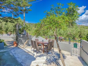A patio with a table and chairs, surrounded by a low wall and a tree.