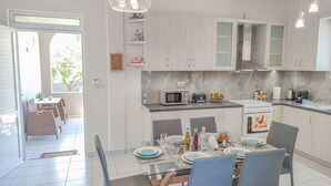 Une cuisine moderne avec des meubles blancs, un coin repas doté d’une table en verre et une vue sur l’extérieur.