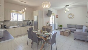 Une cuisine moderne avec un coin repas, un canapé gris et un téléviseur fixé au mur.