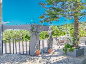 A gated entrance with a pergola, potted plants, and a view of the sea.