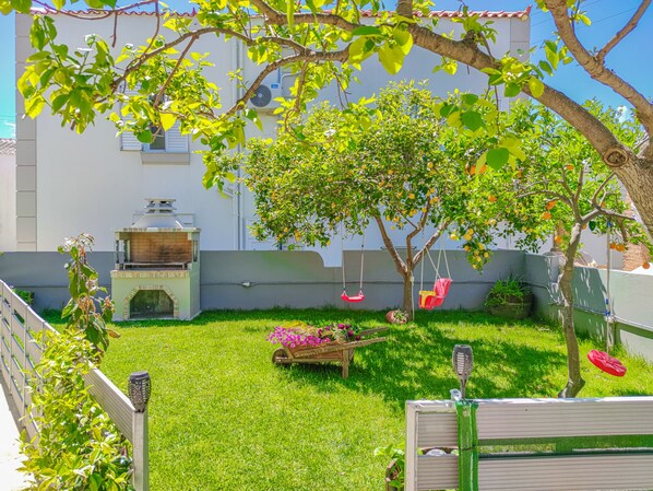 A backyard with a barbecue grill, a swing set, and a tree with hanging chairs.