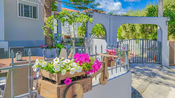 Un chariot en bois décoré de fleurs, un mur blanc et un portail en métal.