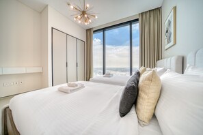 A hotel room with a large bed, a wardrobe, a view of the city, and a modern chandelier.
