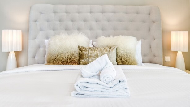 A neatly made bed with a tufted headboard, two fluffy pillows, and a stack of folded towels. - Cityscape and Majestic Retreat at Address JBR (Dubai)