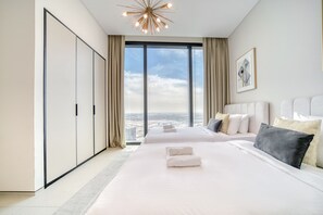 A modern hotel room with a large bed, a view of the city, and a wardrobe.