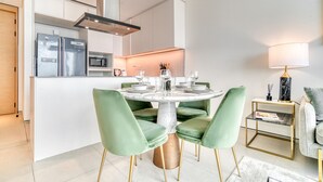 A modern kitchen with a central island, stainless steel appliances, and a dining area with green upholstered chairs. - Cityscape and Majestic Retreat at Address JBR (Dubai)