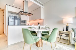 A modern kitchen with a central island, stainless steel appliances, and a dining area with green upholstered chairs. - Cityscape and Majestic Retreat at Address JBR (Dubai)