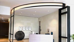 Un área de recepción moderna con un mostrador curvo, un jarrón decorativo grande y obras de arte enmarcadas en la pared.