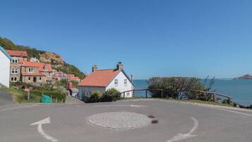 Eine Küstenstraße mit Kreisverkehr, Häuser mit roten Dächern und freiem Blick auf das Meer.