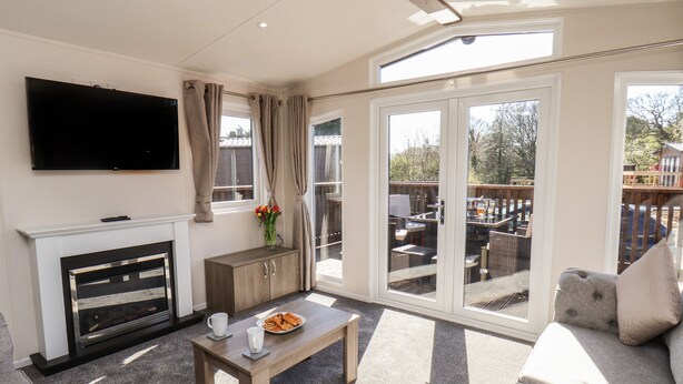 A living room with a fireplace, a flat-screen TV, a dining area with outdoor seating, and large sliding glass doors. - Foxglove Lodge (Saltburn-by-the-Sea)