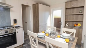 A modern kitchen with white cabinetry, a built-in stove, and a dining area with a table set for four. - Foxglove Lodge (Saltburn-by-the-Sea)