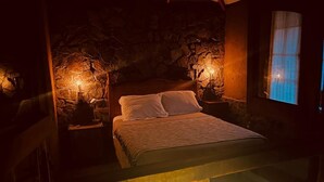 Un dormitorio acogedor con pared de piedra, una cama con ropa de cama blanca y una mesita de noche con lámpara.