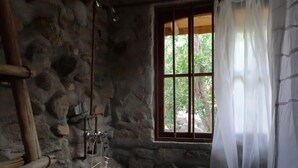 Una habitación rústica de piedra con una escalera de madera, una ventana con marco de madera y un perchero con botellas.