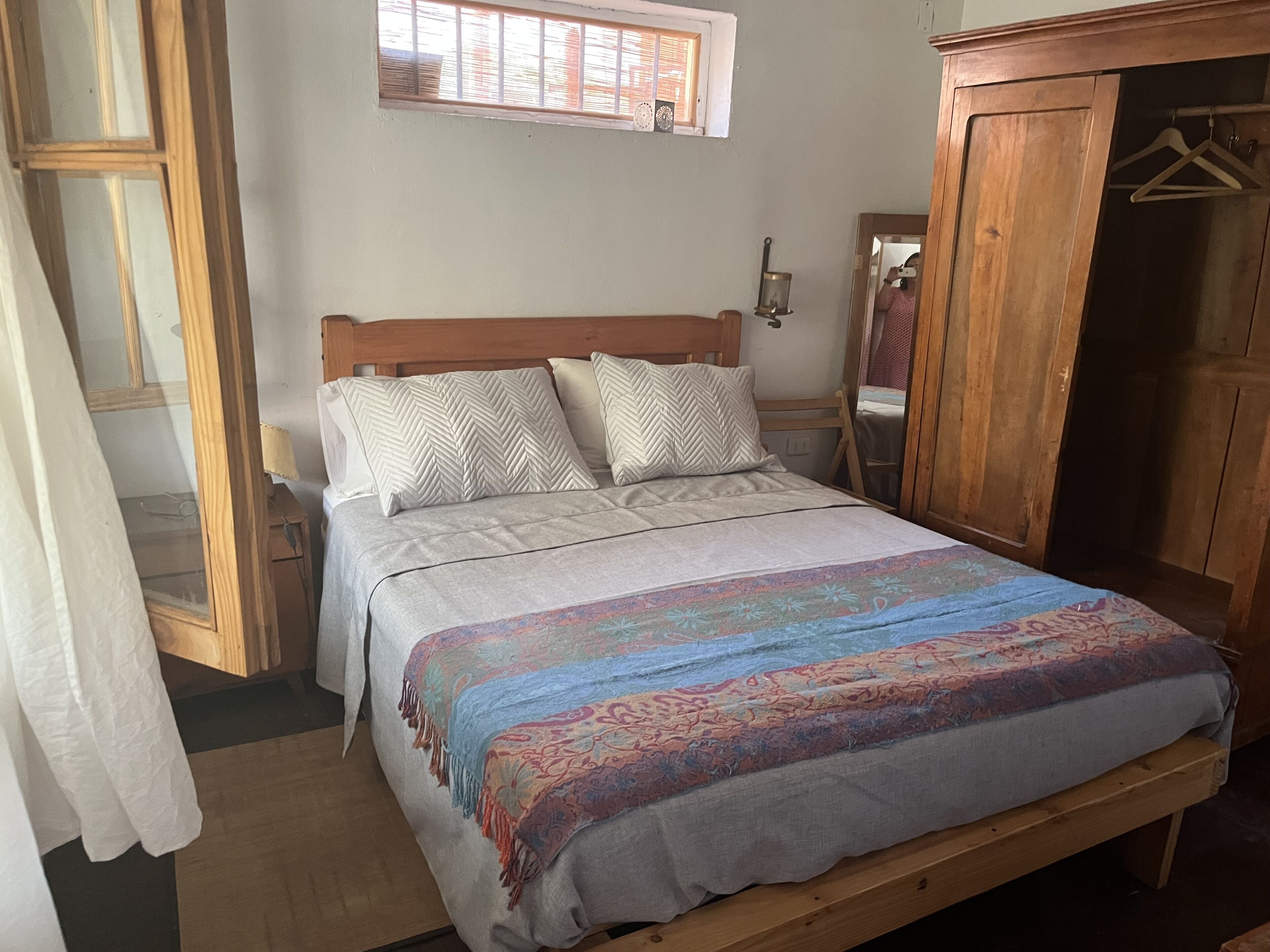 Una cama con una colcha estampada, un cabecero de madera y dos almohadas decorativas.