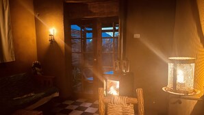 Una habitación acogedora con piso a cuadros, una mesa de madera, una cesta tejida, una lámpara encendida y vistas al exterior a través de una puerta.