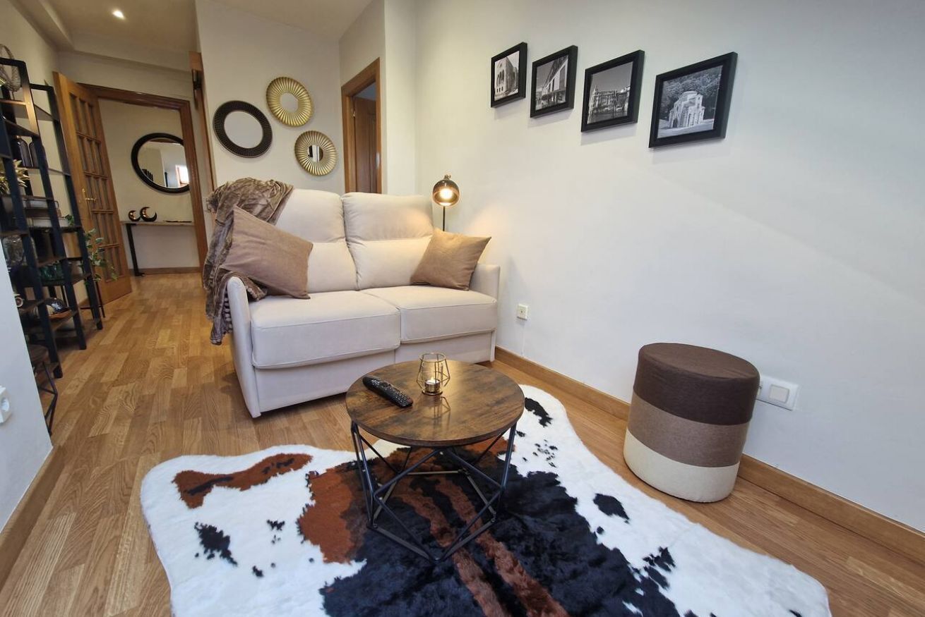 Un salon comprenant un canapé, une table basse ronde, un tapis en peau de vache, une lampe et un tabouret.