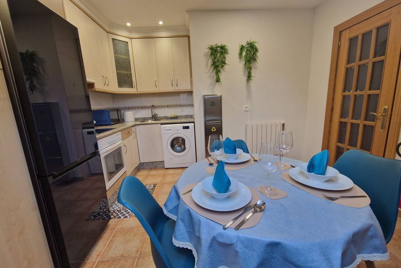 A dining area with a table set for two, a washing machine, and cabinets in the background.