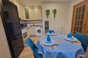 A dining area with a table set for two, a washing machine, and cabinets in the background.