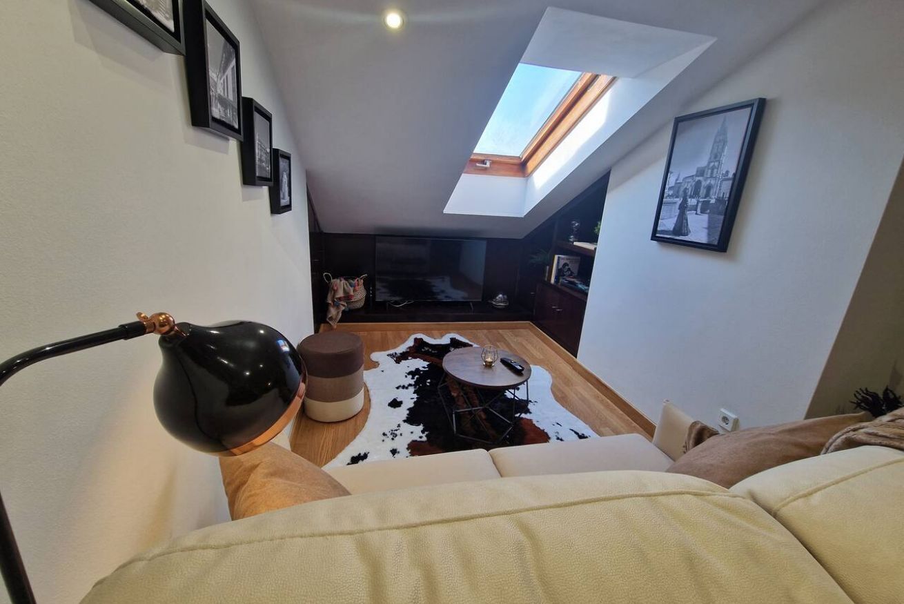 Een moderne woonkamer met dakraam, een bank, een salontafel en een koperen vloerkleed.