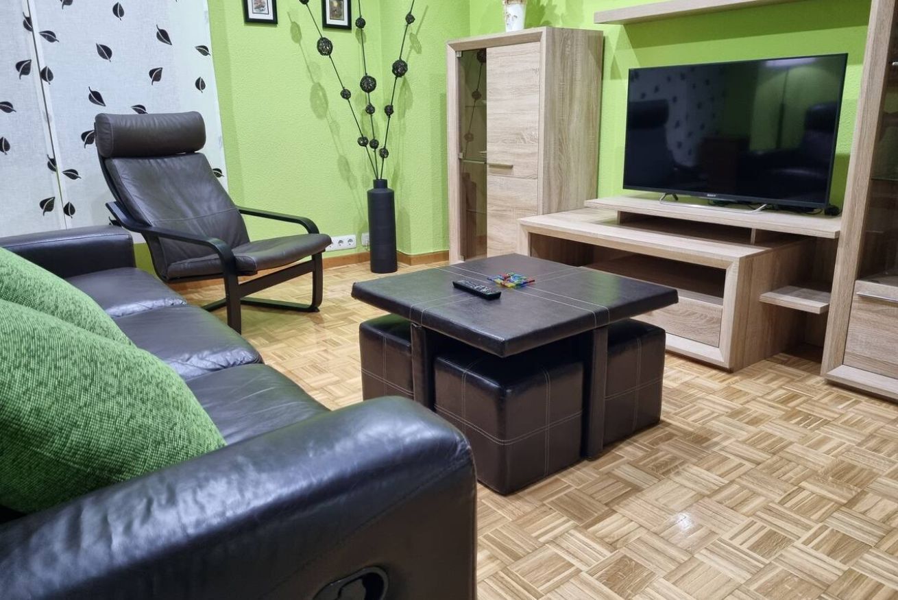 A living room with a sofa, a chair, a coffee table, a TV on a stand, and a decorative plant.