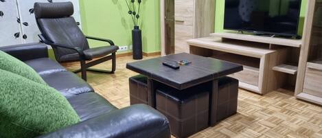 Una sala de estar con sofá, sillón, mesa de centro, televisor sobre un mueble bajo y una planta decorativa.