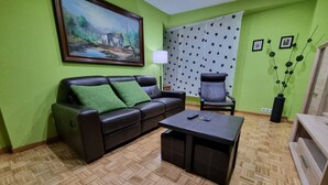 Un salon comprenant un canapé, un fauteuil, une table basse, un tableau au mur et un rideau à motifs.