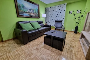 A living room with a sofa, a chair, a coffee table, a painting on the wall, and a patterned curtain. - 126B Apto Playa - 3 Bedrooms by R2R Consulting (Gijón)