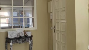 Una habitación con un ventanal grande, una puerta y una pequeña mesa con papeles y un objeto decorativo.