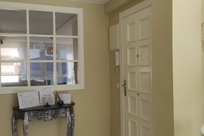 Una habitación con un ventanal grande, una puerta y una pequeña mesa con papeles y un objeto decorativo.