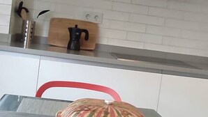 Una cocina con armarios blancos, una silla roja, una tabla de cortar de madera y una cafetera.